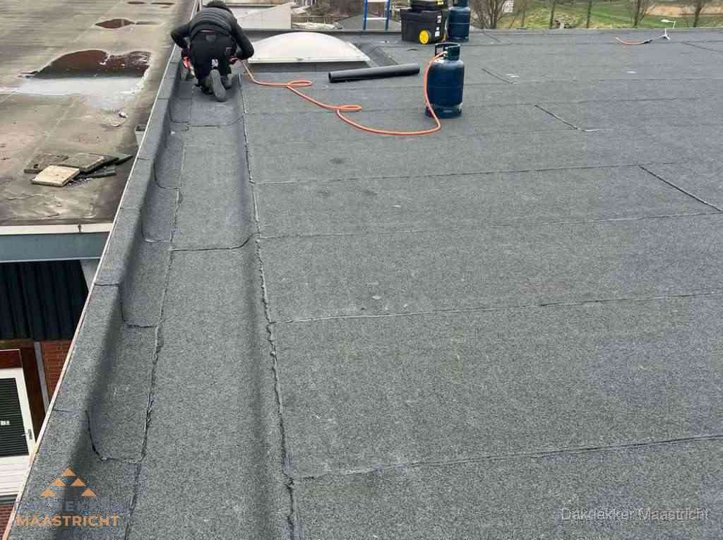 Dakdekker repareert bitumen dakbedekking op groot plat dak in Maastricht